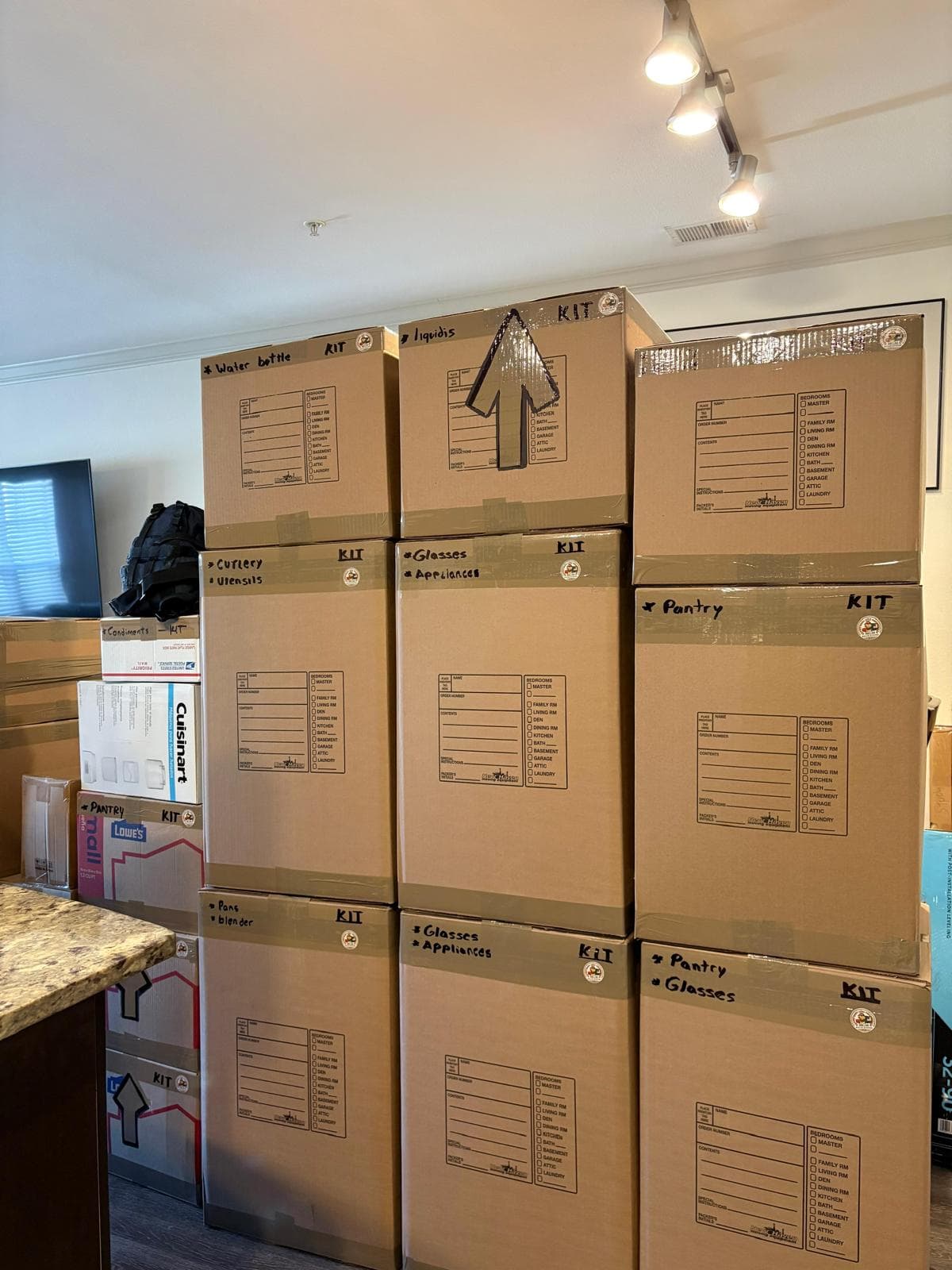 Stacked cardboard moving boxes labeled with kitchen items like pantry, glasses, and appliances.