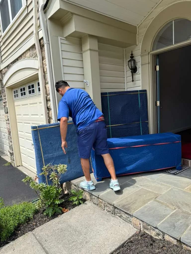 Man in blue moving furniture wrapped in protective blankets on a stone front porch.