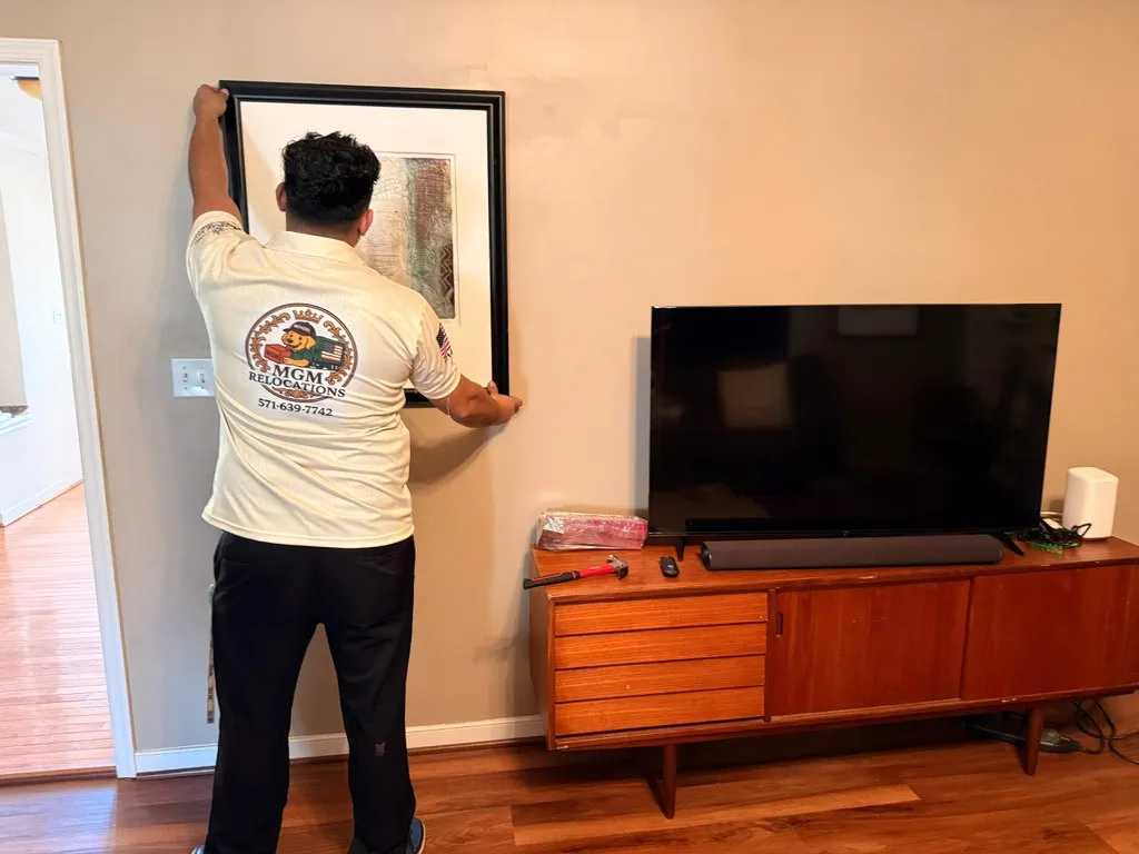 Professional mover hanging a framed picture on a wall next to a wooden media console.