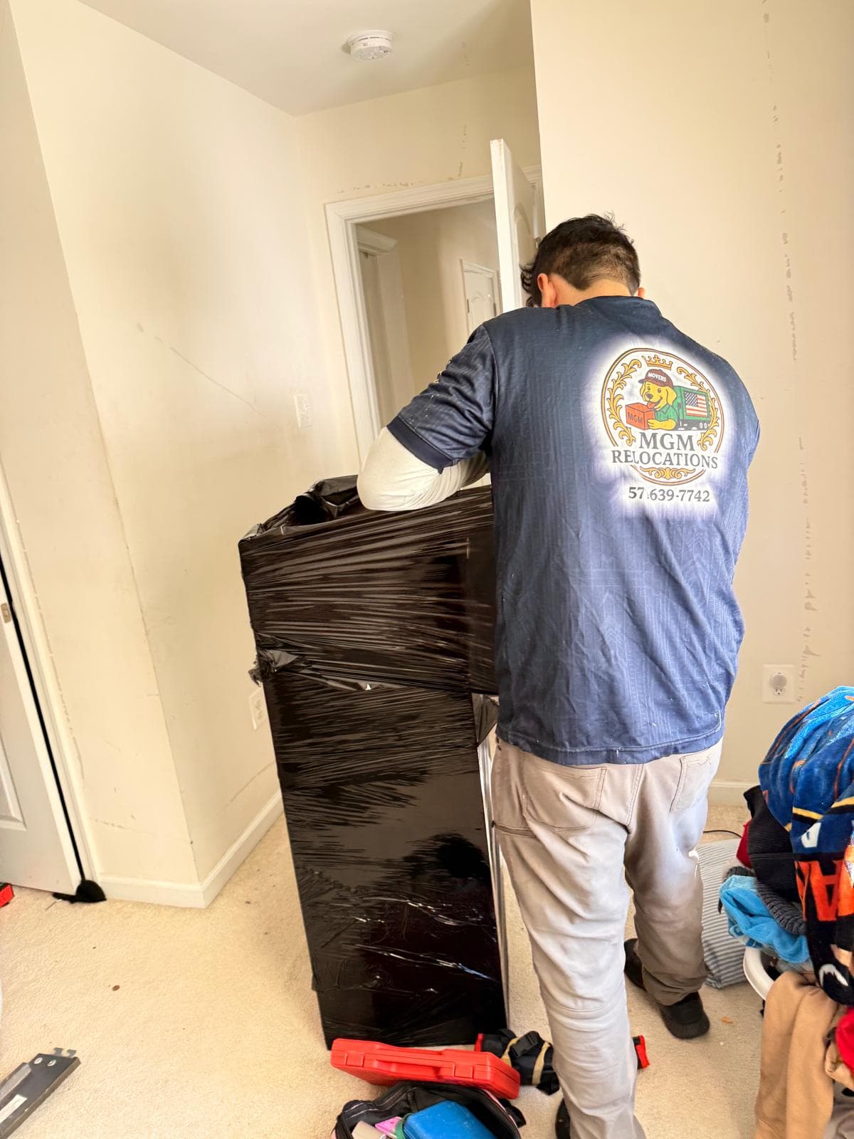 Mover from MGM Relocations wraps a large piece of furniture in black plastic stretch film.