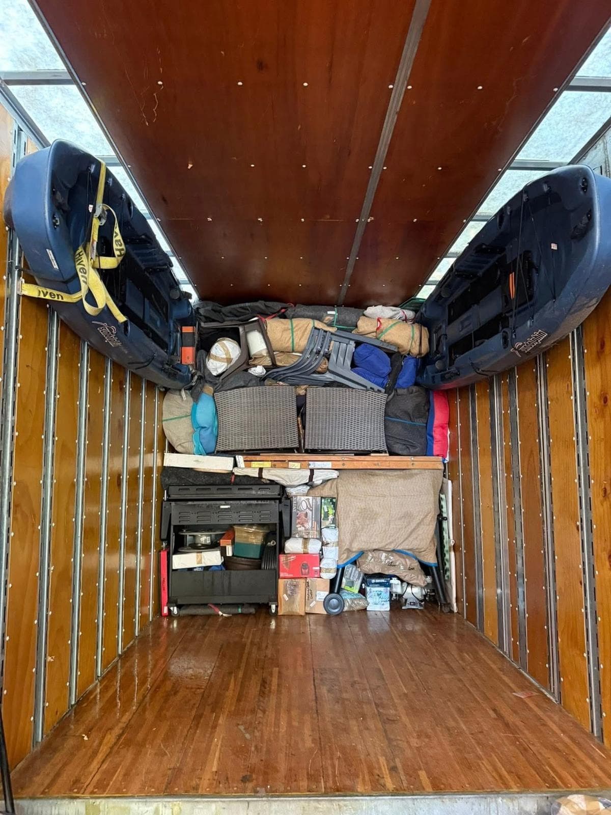 Two blue kayaks strapped to the walls of a moving truck filled with household items.