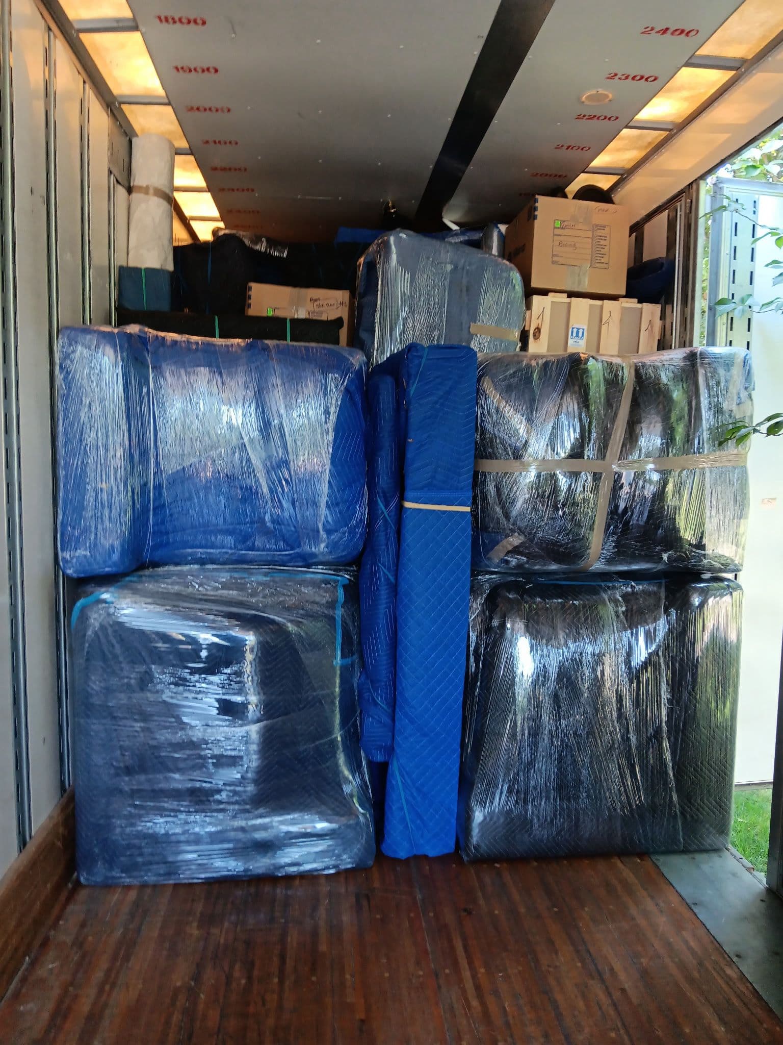 Furniture wrapped in blue protective blankets and plastic film packed inside a moving truck.