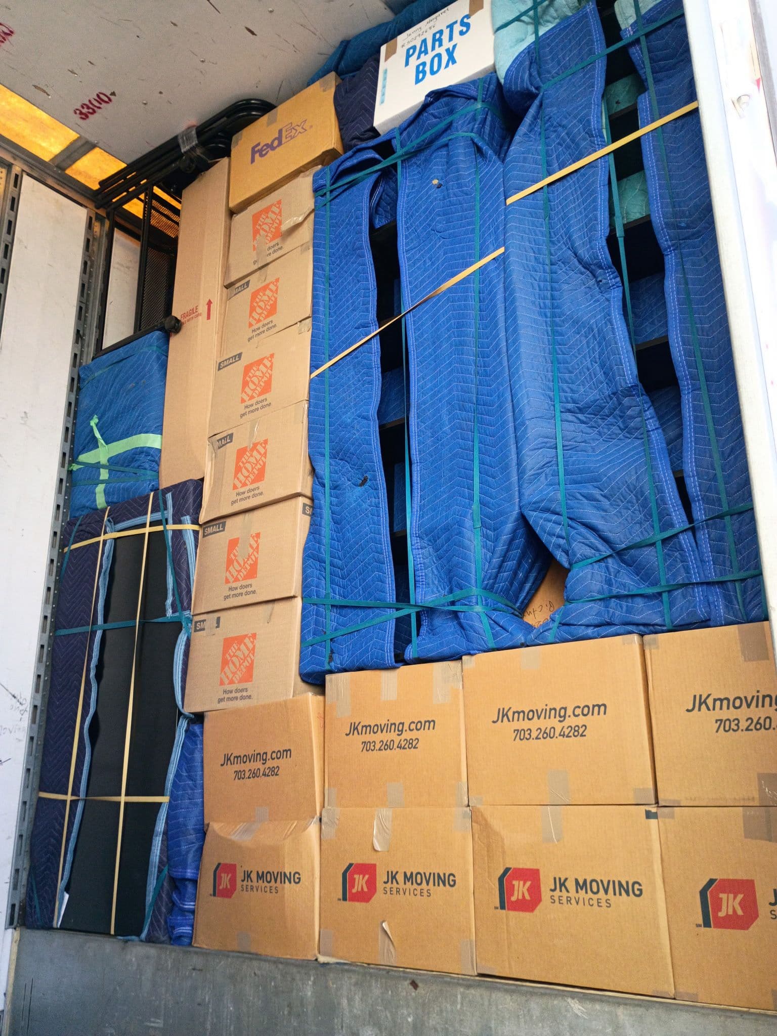 Organized moving truck interior with stacked boxes and furniture protected by blue moving blankets.
